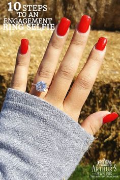 a woman's hand with red nail polish and a ring on her finger, in front of hay bales