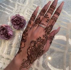 a woman's hand with henna tattoos on it and flowers in the background