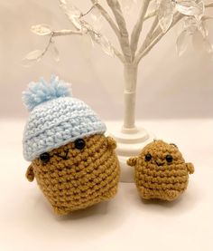 two small crocheted stuffed animals sitting next to a tree with snow on it