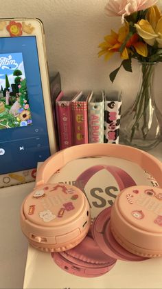 two pink headphones sitting on top of a table next to a laptop and flowers