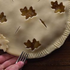 a person holding a fork and looking at a pie with leaves on it, in front of a wooden table