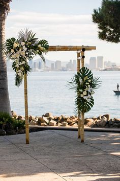 an outdoor ceremony set up by the water with flowers and greenery in front of it