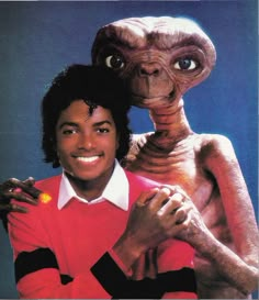 the man is posing with an alien in front of him and another creature behind him