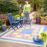 a woman standing next to two blue lawn chairs on top of a colorful area rug