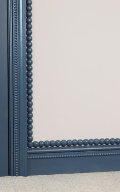 a blue framed mirror with beaded trim on the edges and an empty wall behind it