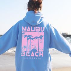 Embrace the laid-back vibes of Malibu with our Malibu Beach Hoodie. This soft blue sweatshirt features a stylish, vintage-inspired Malibu Beach print. The design showcases palm trees with a sunset beach scene, bringing a touch of tropical paradise to your everyday wear. This hoodie is perfect for beach lovers, travelers, and anyone who loves to stay cozy while looking effortlessly cool. The classic fit suits both men and women, ensuring maximum comfort and style. WHY YOU'LL LOVE IT ✅ Comfy: This Blue Hooded Beach Tops, Vacation Hoodie With Relaxed Fit And Long Sleeves, Blue Hooded Tops For Beach, Blue Hooded Top For Beach, Blue Hooded Tops For The Beach, Hooded Cotton Top For Vacation, Cotton Hooded Top For Vacation, Relaxed Fit Long Sleeve Hoodie For Vacation, Oversized Hooded Top For Vacation