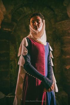 a woman dressed in medieval clothing standing next to a stone wall with her hands on her hips