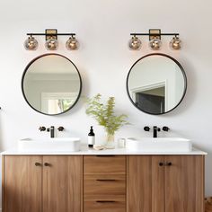 two mirrors on the wall above double sinks in a bathroom with wood cabinets and white walls