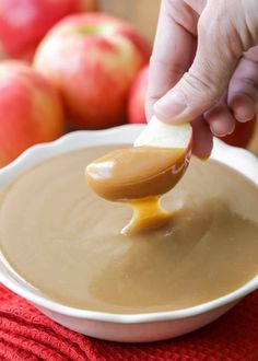 a spoon full of caramel sauce being dipped into a bowl with apples in the background