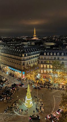 a christmas tree is lit up in the middle of a city square with cars and people around it