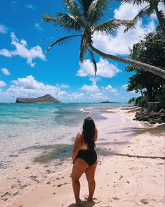 a woman is standing on the beach looking at the water and palm trees in the distance