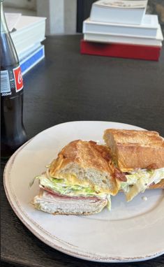 a sandwich cut in half sitting on top of a white plate next to a bottle of soda