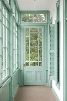 an empty hallway with green painted doors and windows on both sides, leading to the front door