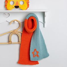 an orange and blue knitted scarf next to a pair of scissors on a white shelf