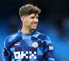 a young man in a blue and white shirt smiles at the camera while standing on a soccer field