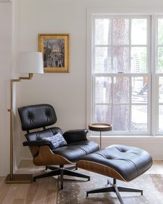 an eames chair and ottoman in front of a window