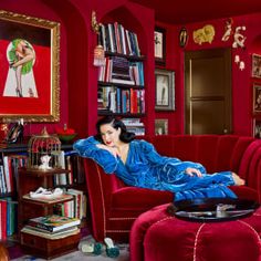 a woman laying on top of a red couch in a living room next to a bookshelf