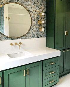 a bathroom with green cabinets and a white counter top under a large round mirror above the sink