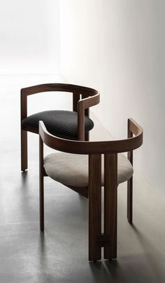 a wooden chair sitting in front of a white wall with a black cushion on it