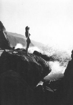 a woman standing on top of a rock next to the ocean