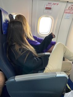 a woman sitting in an airplane seat with her feet up on the ground and looking out the window