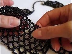 two hands are working on a beaded necklace with black beads and silver clasps