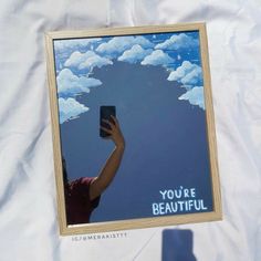 a person holding up a cell phone in front of a poster that says you're beautiful