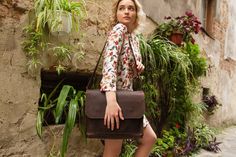 a woman holding a brown bag in front of a wall with potted plants on it