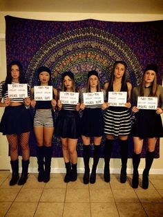 five girls holding up signs in front of a tapestry