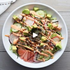 a white plate topped with cucumber, salmon and avocado covered in sauce