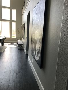 an empty room with wood floors and paintings on the wall in front of windows, along with benches