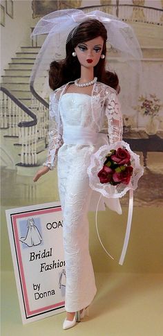 a barbie doll wearing a white wedding dress and veil with flowers in her hand, holding a bridal fashion by donna sign