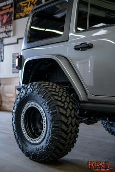 the front end of a white jeep with large tires and rims in a garage