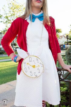 a woman in a white dress and red jacket with a clock on her chest is posing for the camera