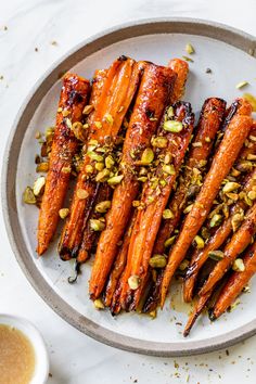 roasted carrots with pistachio seeds on a plate next to a cup of sauce