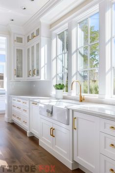 a large kitchen with white cabinets and gold hardware on the handles, windows, and sink