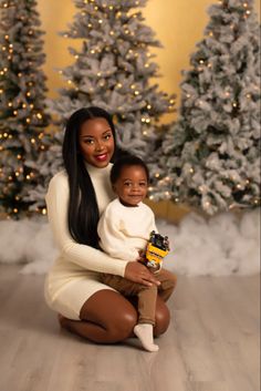 a woman is holding a baby in front of christmas trees with lights on the background