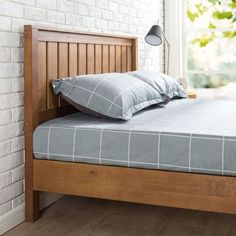 a wooden bed frame with two pillows on it and a lamp next to the headboard