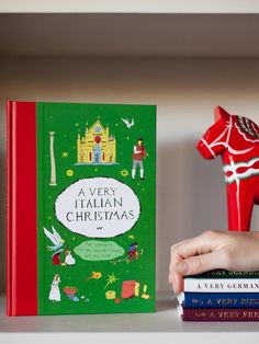 a person holding a book in their hand next to some books on a shelf and a toy horse