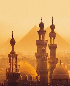 two large buildings with towers in front of the pyramids and cityscape behind them