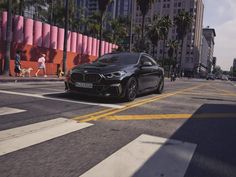 a black car is driving down the street in front of tall buildings and palm trees