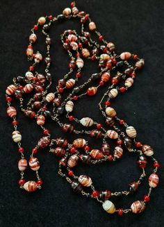 On offer here are two stunning Art Deco necklaces that I would date from around the 1930's There are two strands on offer as I did not really want to separate them as they compliment each other so well.  The long strand (110 cm) is striped agate beads, highly polished and beautifully crafted in a wide range of colours but essentially terracotta through to white with bands of red, brown and gold throughout.  Between each wired bead is a wired carnelian stone. No clasp these are made for layering The slightly 'shorter strand' is 96 cm long and the agate stones are predominately black but with terracotta highlights and flashes of other colours including gold.  In between each wired bead is a small black glass bead. The stones are beautiful and each one is different and the necklaces look wond Vintage Double Strand Necklaces For Formal Occasions, Antique Brown Necklace For Collectors, One Of A Kind Vintage Brown Jewelry, Vintage Single Strand Round Necklace, Vintage Beaded Chain Necklaces, Vintage Round Bead Necklaces Collectible, Vintage Multi-strand Beaded Necklace With Polished Beads, Vintage Necklaces With Polished Beads For Gifts, Antique Jewelry With Round Beads For Vintage Collection