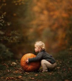 a little boy sitting on the ground with a pumpkin in his lap and looking at it