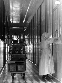 black and white photograph of two women in long dresses, one pushing a cart with items on it