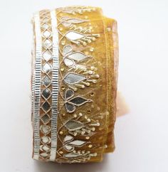 a close up of a bracelet on a white surface with gold and silver trimmings