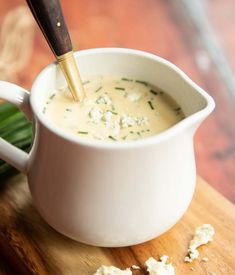 a white pitcher filled with soup sitting on top of a wooden cutting board