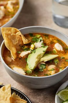 a bowl of soup with tortilla chips and avocado on the side