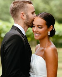 a bride and groom kissing each other outside