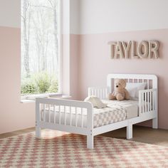 a teddy bear sitting on top of a white bed in a pink and white bedroom