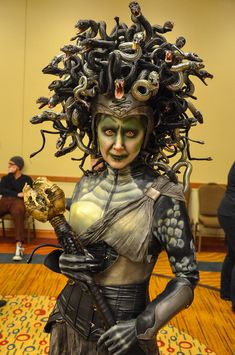 a woman dressed in costume and makeup with snakes on her head, holding a skull